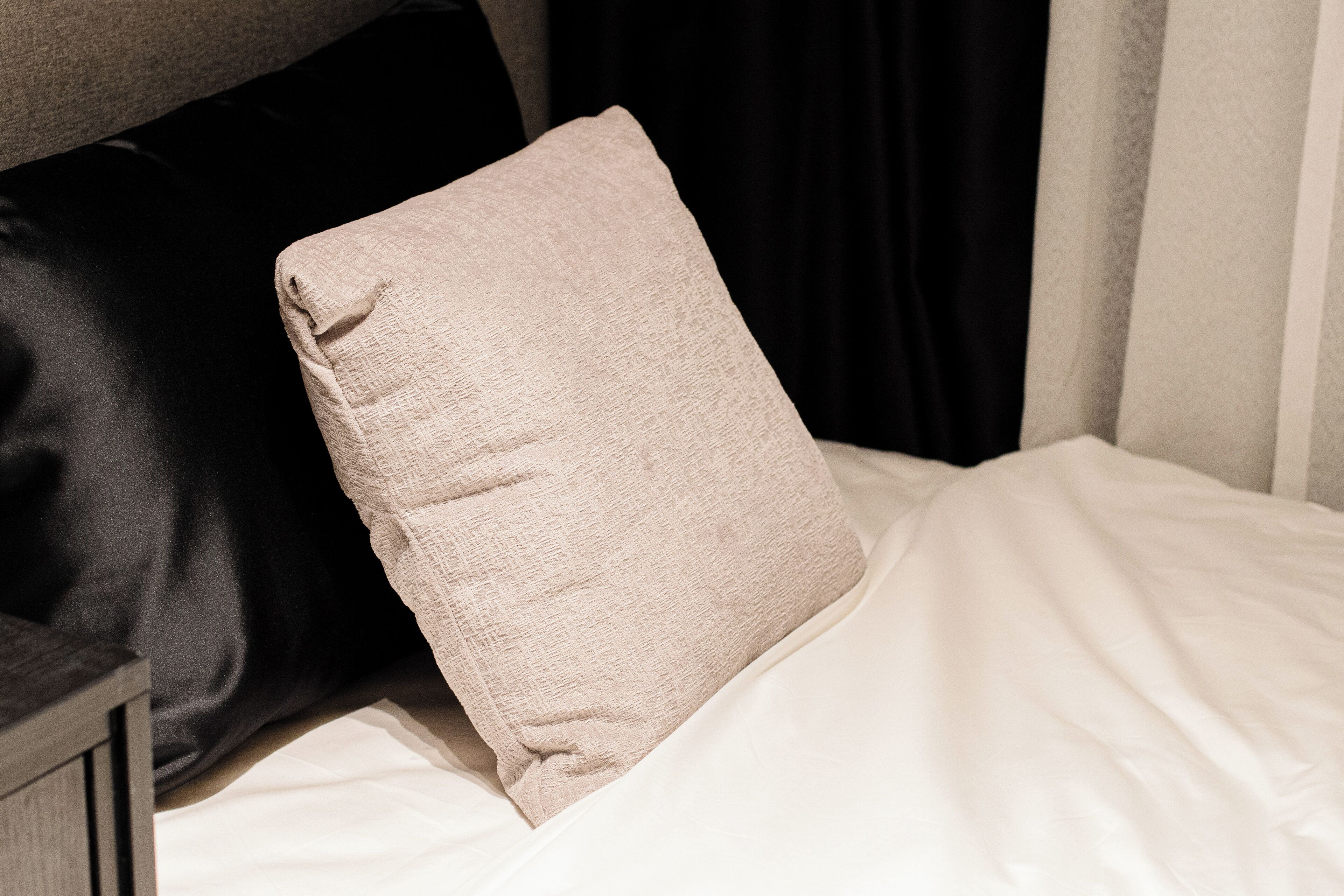 A bed with a beige pillow and a black pillow.