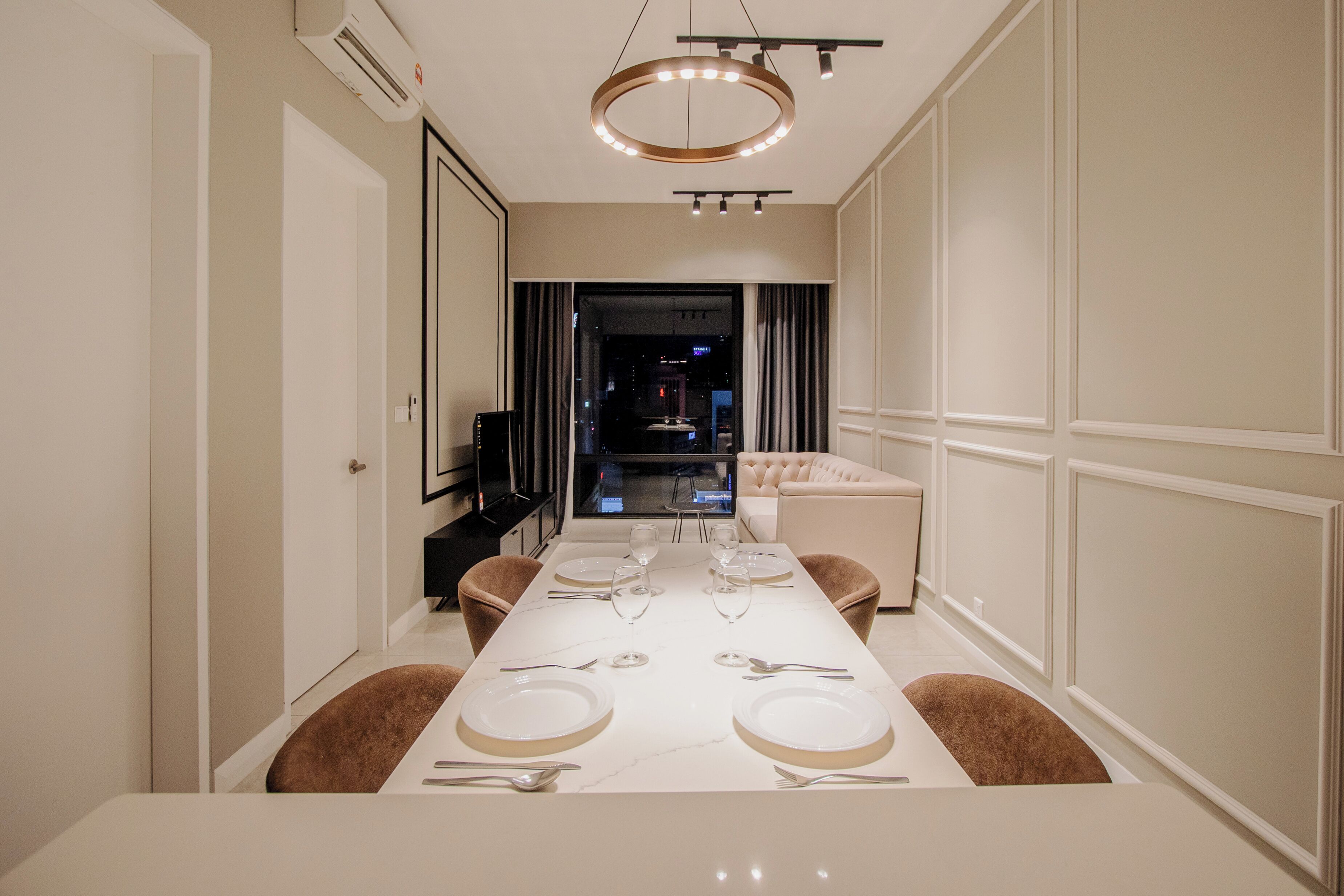 A modern dining room with a long table set for six, a chandelier, and a view into the living area.
