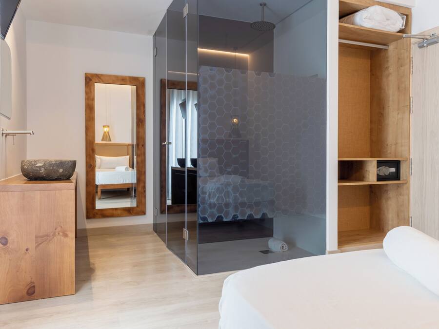 A modern bedroom with a glass shower enclosure, wooden wardrobe, and a bedside table with a bowl.