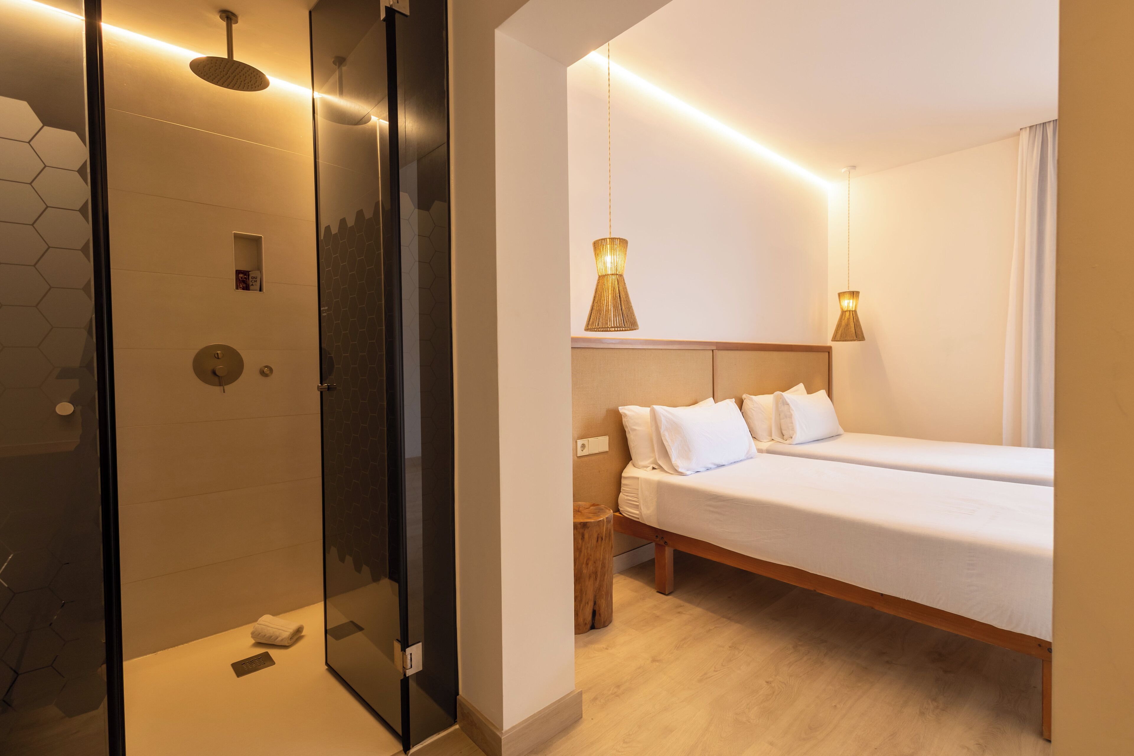 Habitació d'hotel moderna amb un espai de banyera de vidre, un llit amb estructura de fusta i una taula de nit.
