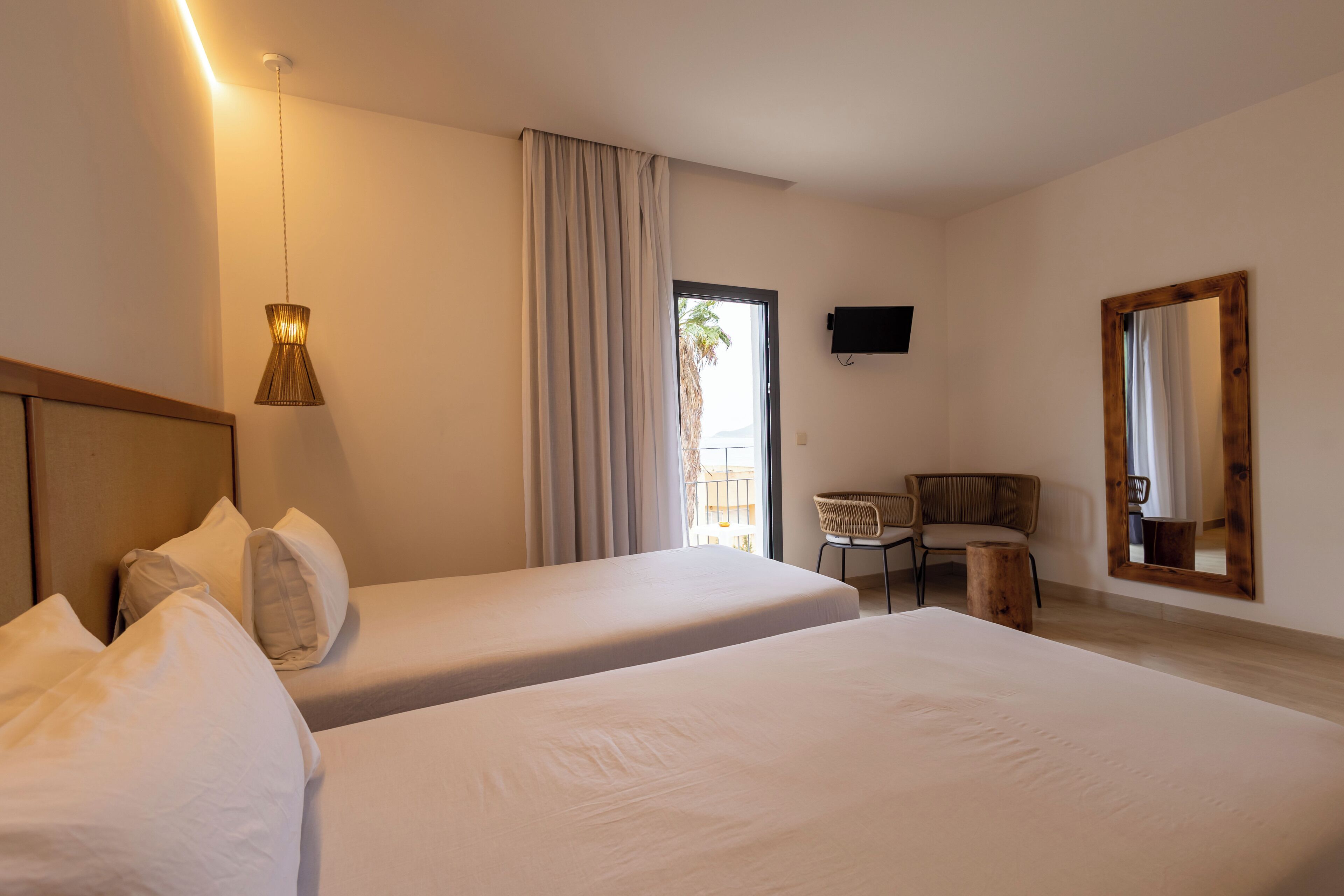 A hotel room with two beds, a desk, a chair, a television, and a large window with curtains.