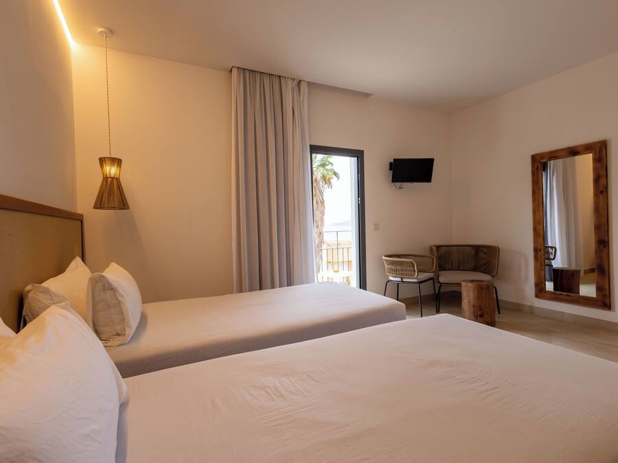 A hotel room with two beds, a desk, a chair, a television, and a large window with curtains.
