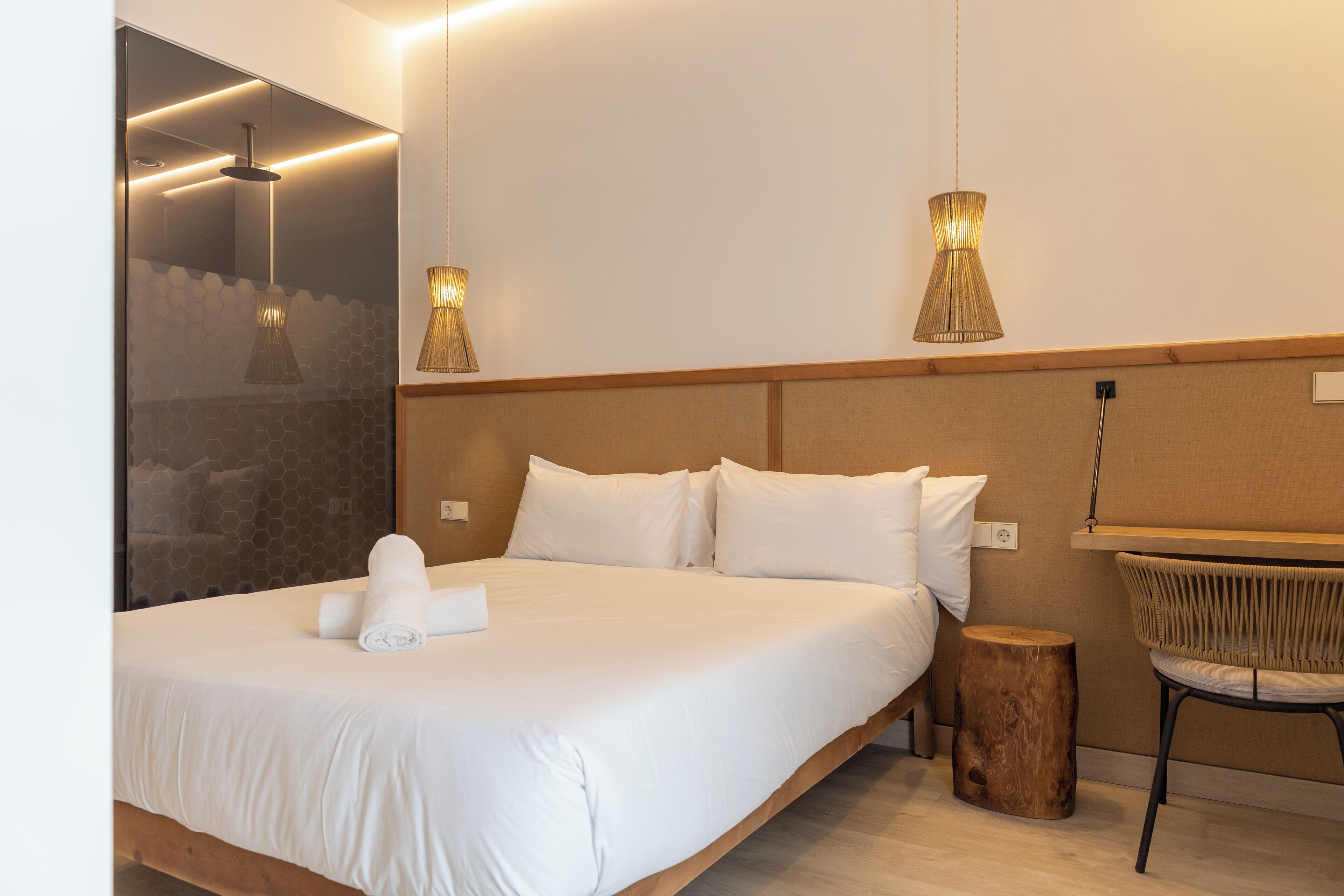 A modern hotel room with a large bed, two wall-mounted lamps, a wooden nightstand, and a wicker chair.