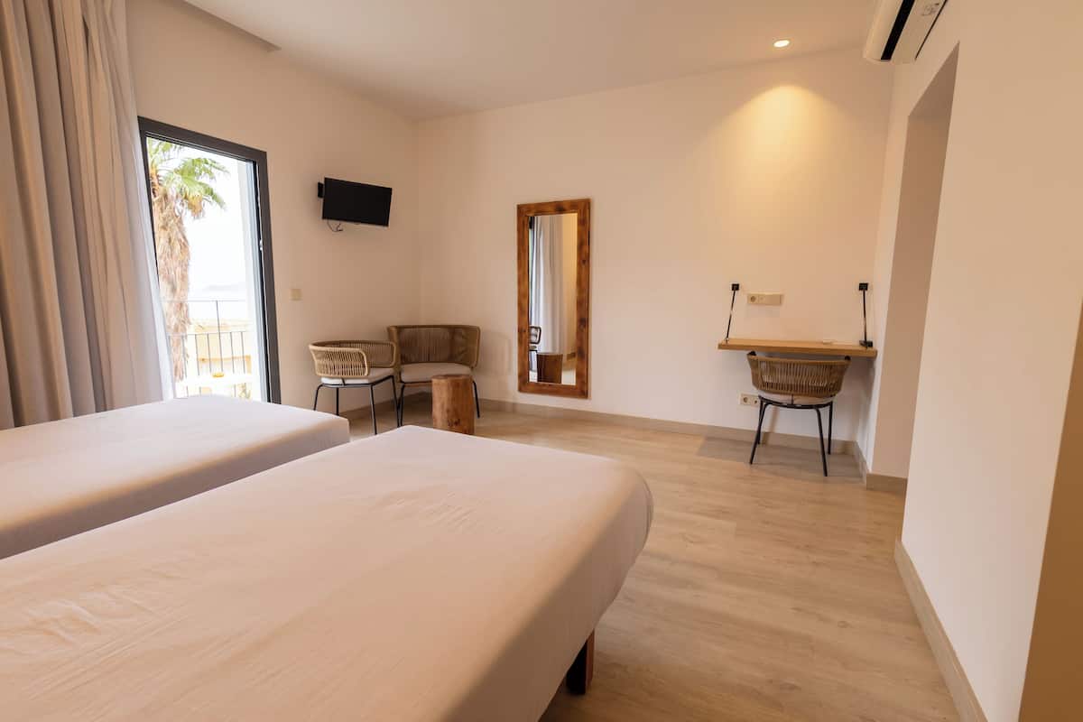 Een hotelkamer met twee bedden, een bureau, een stoel, een spiegel en een televisie aan de muur.