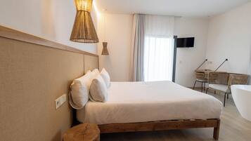 Un dormitorio con cama de madera, lámpara de noche, televisor montado en la pared y ventana con cortinas.