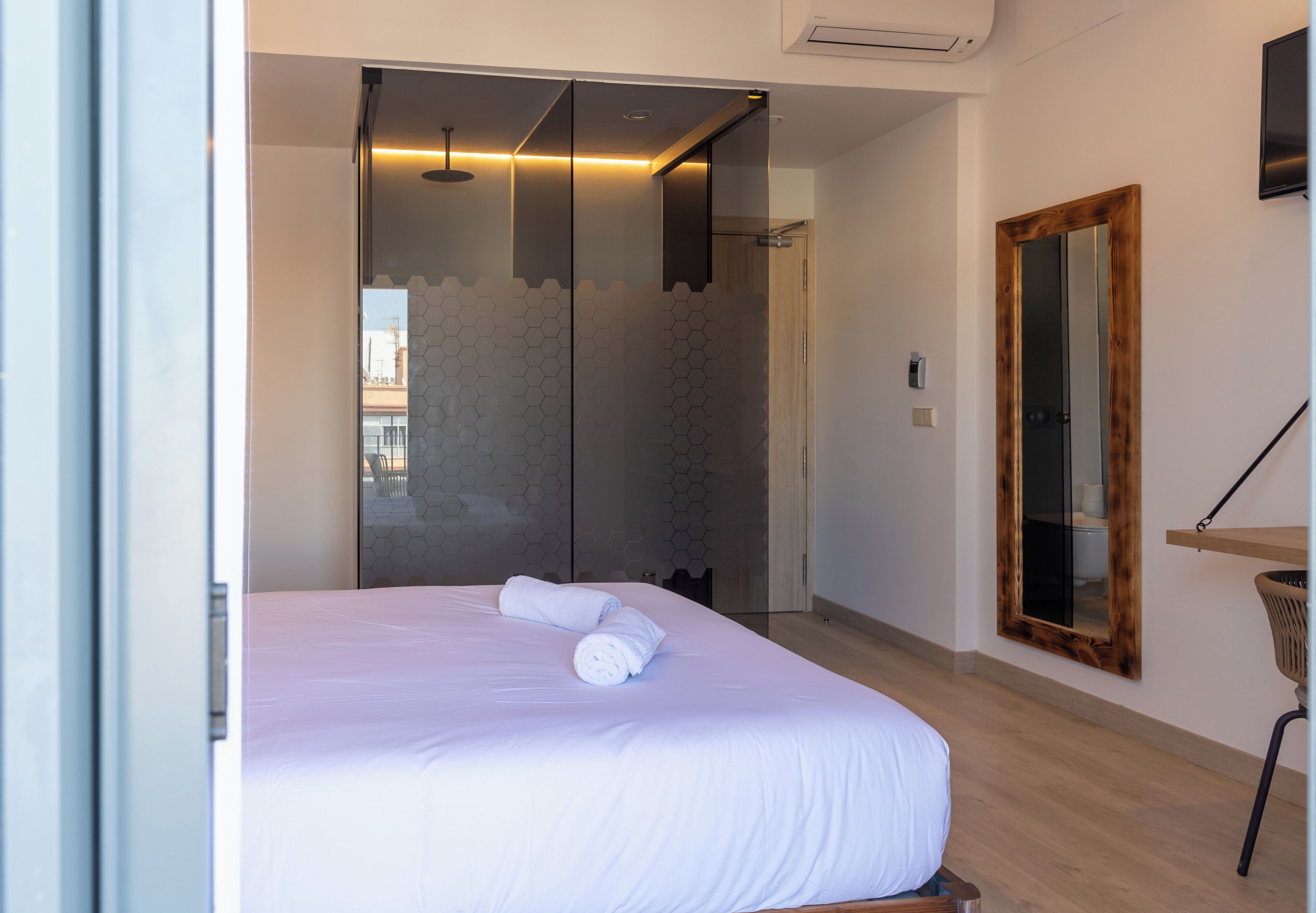 A modern hotel room with a large bed, a shower area, and a wooden-framed mirror.