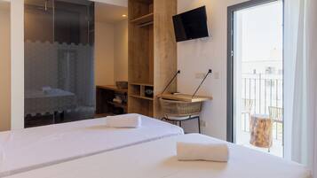Habitación de hotel con dos camas, zona de ducha, televisor montado en la pared y balcón con sillas.