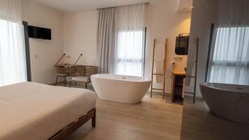 Una habitación de hotel moderna con una cama grande, una bañera independiente, un escritorio con una silla y un televisor montado en la pared.