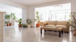 A spacious living room with a beige sofa, a wicker coffee table, and several potted plants. - Play Hotel Ibiza (Ibiza Town)