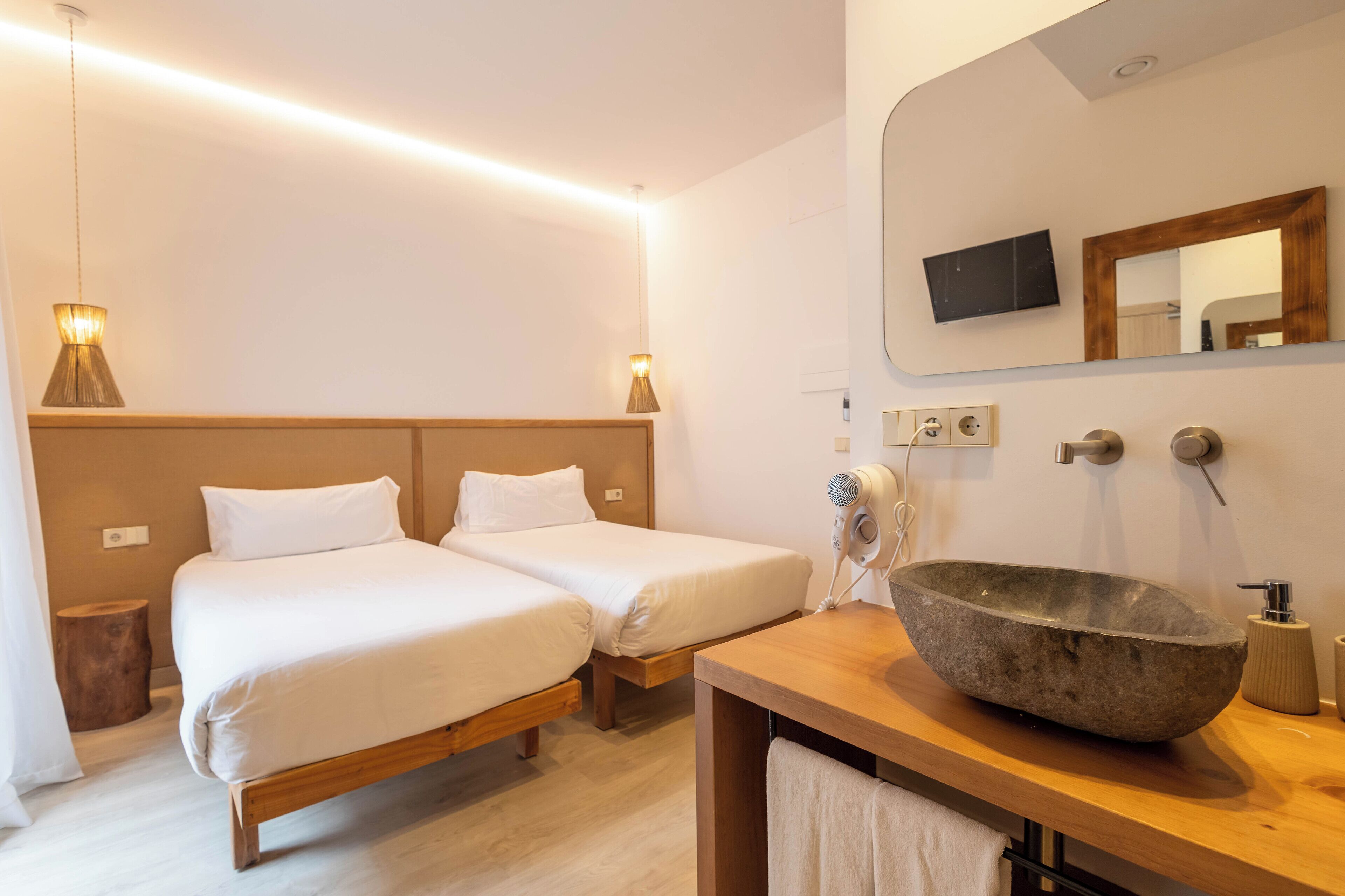 Una camera d'albergo con due letti singoli, una testiera in legno, un lavandino in pietra e uno specchio sopra il lavandino.