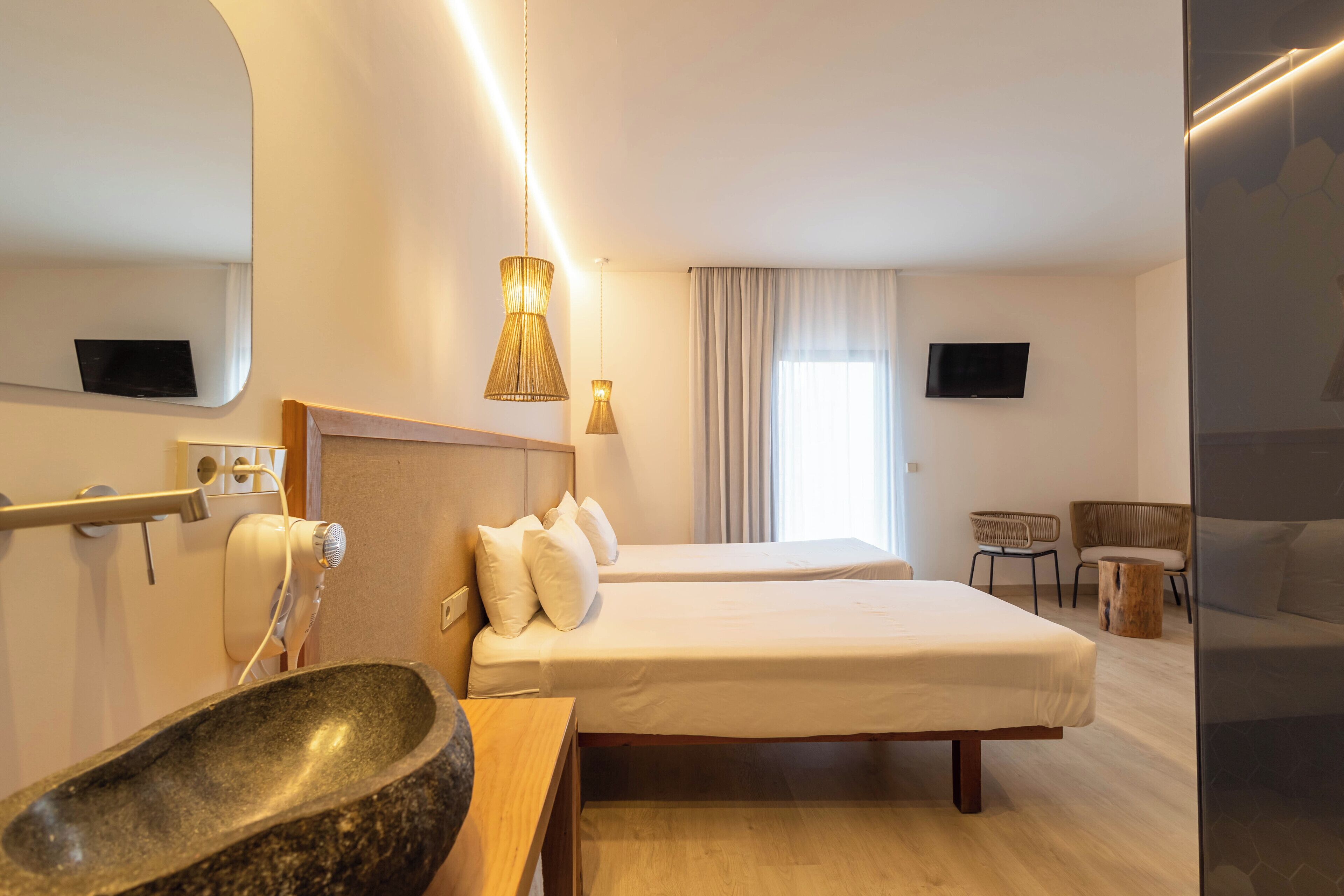 Habitación de hotel con dos camas, un lavamanos grande, un espejo, un televisor y una ventana con cortinas.