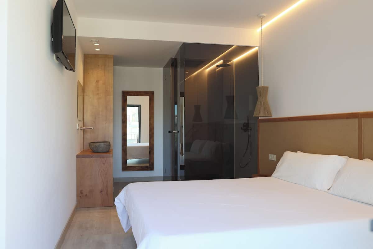 Een moderne hotelkamer met een groot bed, een houten kast, een spiegel en een douchecabine van glas.