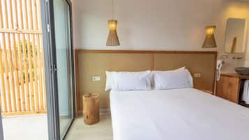 A bedroom with a large bed, wooden headboard, two pendant lights, a wooden stool, and a sliding glass door leading to an outdoor area.