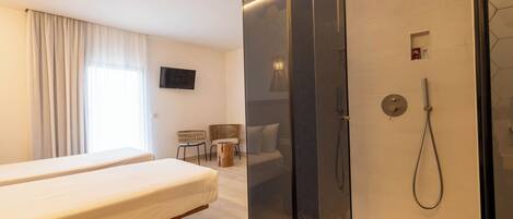A hotel room with a bed, a shower area, a TV, and a seating area with chairs.