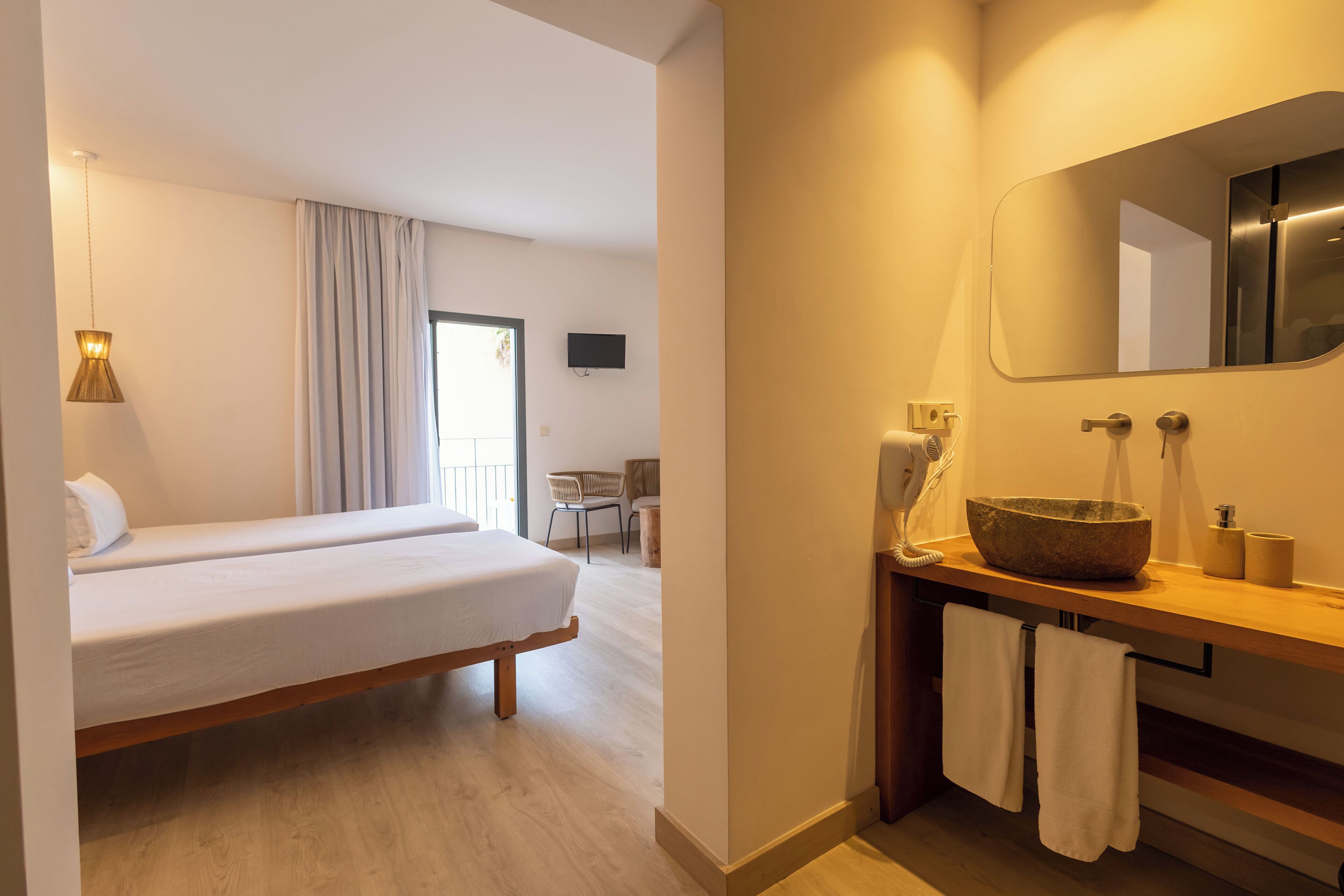A hotel room with a bed, a wooden nightstand with a basin, towels, and a television on the wall.