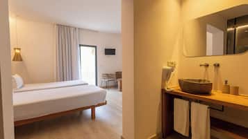 Une chambre d’hôtel avec un lit, une table de chevet en bois sur laquelle se trouve un lavabo, des serviettes et un téléviseur fixé au mur.
