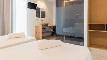 Une chambre d’hôtel moderne équipée de deux lits, d’un bureau en bois, d’un grand miroir, d’une télévision et d’un espace douche doté d’une porte en verre.