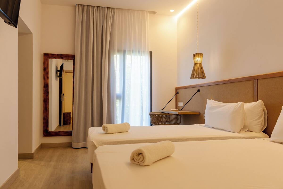 Een hotelkamer met twee bedden, een spiegel, een lamp en een raam met gordijnen.