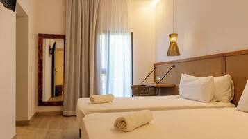 Une chambre d’hôtel avec deux lits, un miroir, une lampe et une fenêtre avec des rideaux.