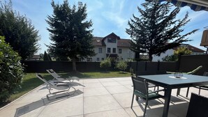 A patio with a table and chairs, a trash bin, and a view of a house and trees.