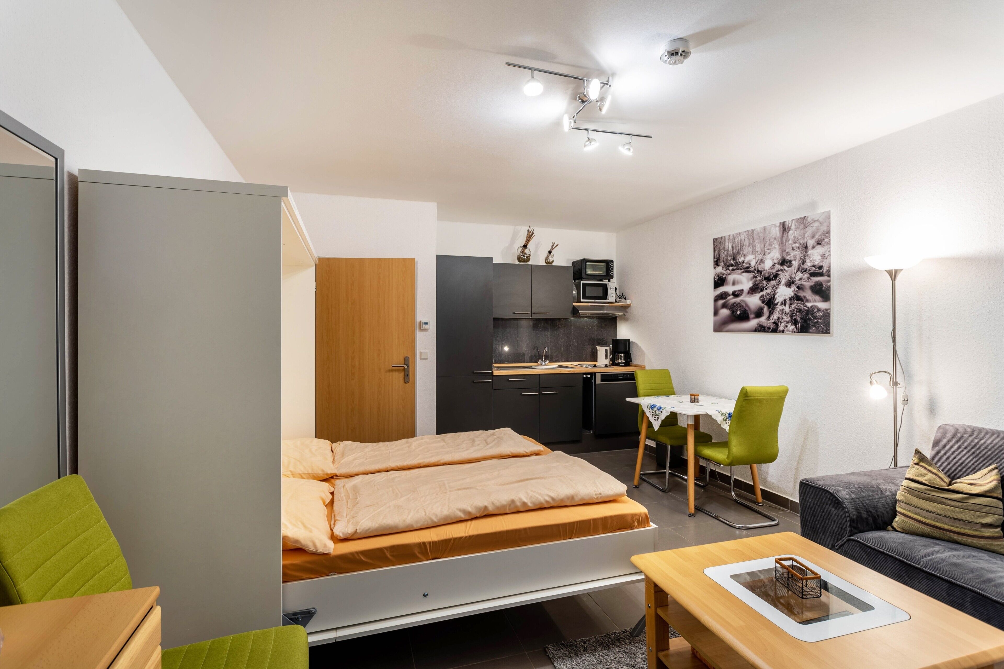Ein kompakter Raum mit Bett, Schreibtisch, Sofa, Küchenzeile und Essbereich.