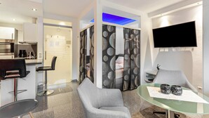A modern hotel room with a kitchen, a dining area, a TV, and a seating area with a glass table. - Apartment 'Gästehaus Centrum 2 Typ 08' with Mountain View, Balcony and Wi-Fi (Willingen (Upland))