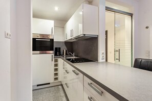 Une cuisine moderne avec des meubles blancs, un four en acier inoxydable, une cuisinière à gaz et une machine à café noire.
