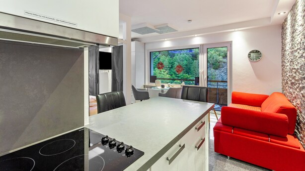 A compact kitchen with a dining area, a red sofa, and a large window with a view of greenery. - Apartment 'Gästehaus Centrum 2 Typ 08' with Mountain View, Balcony and Wi-Fi (Willingen (Upland))