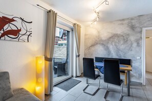 A modern room with a dining table, chairs, a sofa, a floor lamp, and a view through a glass door.