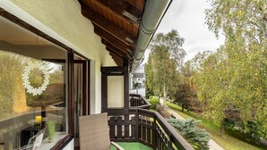 Un balcón con vista a un jardín, una silla de mimbre y una mesa con un mantel individual.