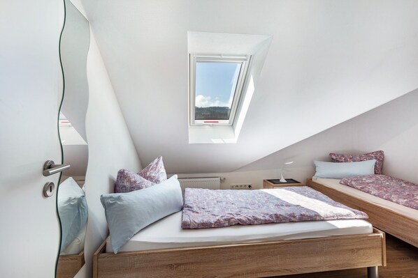 Une chambre avec un puits de lumière, deux lits, un radiateur et une tête de lit en bois.