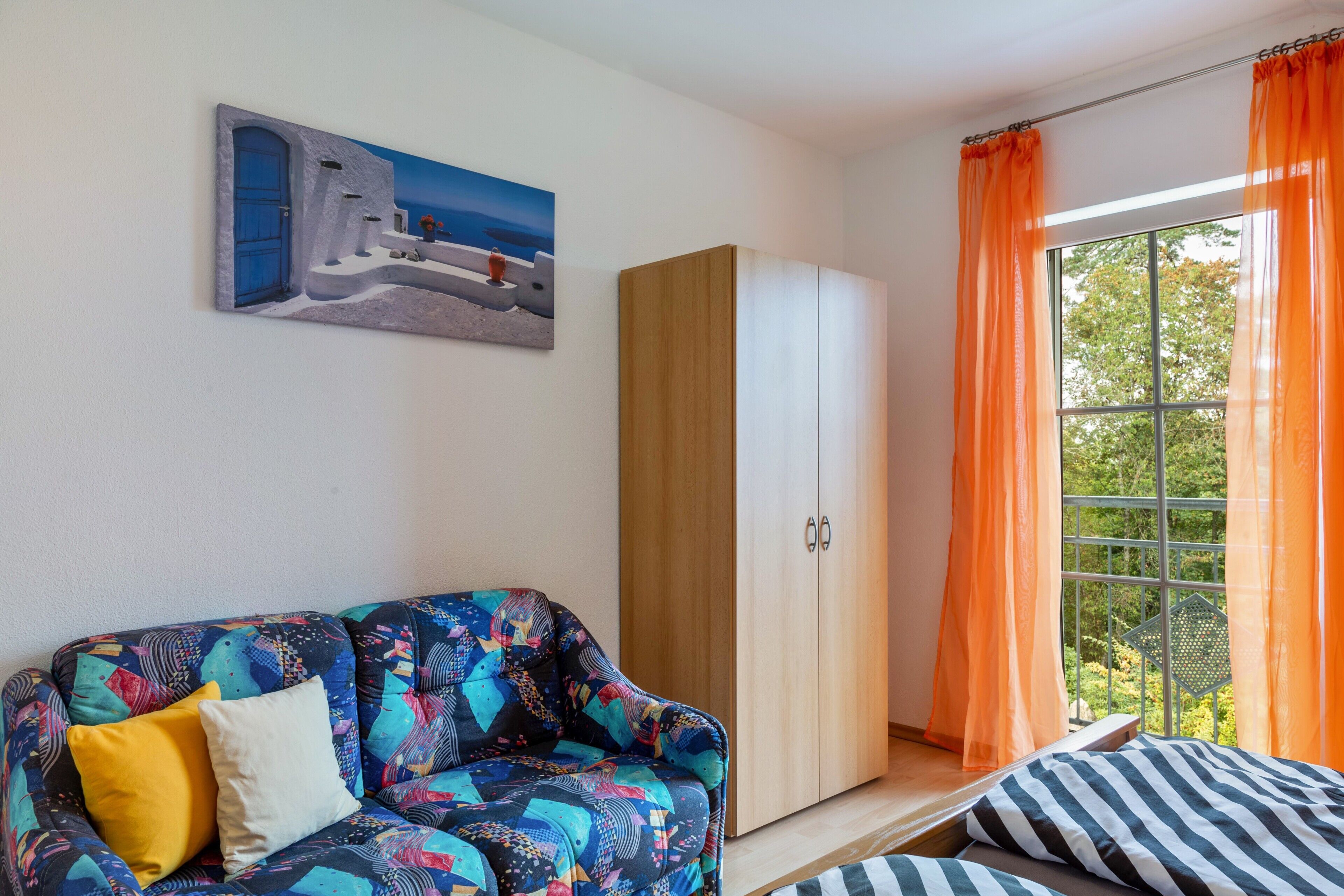 A room with a sofa, a wardrobe, a window with curtains, and a painting on the wall.