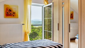 A bedroom with a bed, a window with curtains, a radiator, and a view of greenery.