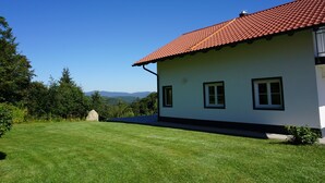 A white building with a red-tiled roof, a grassy lawn, and a clear blue sky.