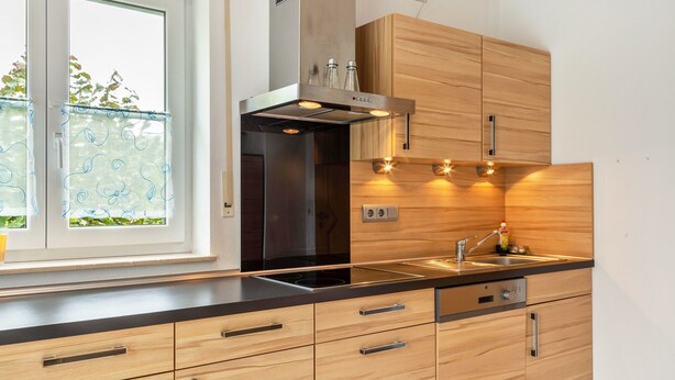 A modern kitchen with wooden cabinets, a stainless steel range hood, and a window with decorative glass.