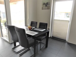 Un coin repas comprenant une table, quatre chaises, un panier de fruits et une vue à travers la porte vitrée.