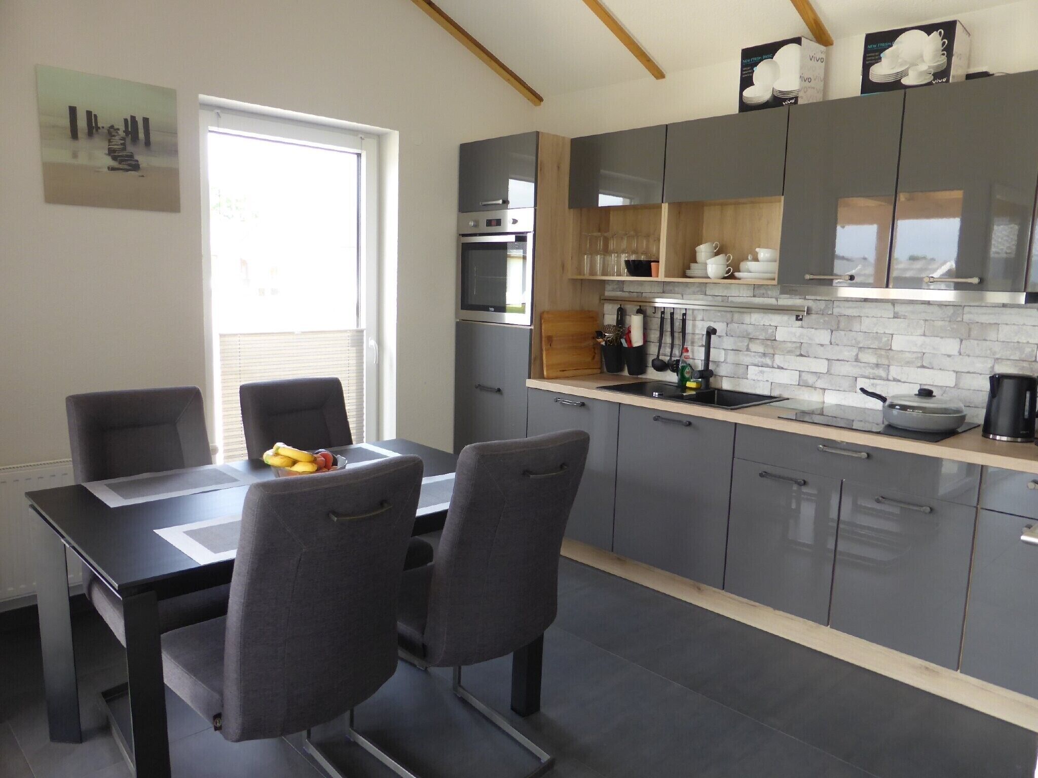 A modern kitchen with grey cabinets, a wooden countertop, and a dining area with a table and chairs.