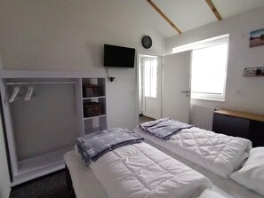 Une chambre avec deux lits, une armoire, une télévision et une fenêtre.