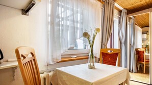 Une pièce avec une table, des chaises, une fenêtre avec des rideaux et une vue sur une autre pièce.