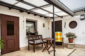 Un patio con un banco de madera, una mesita, una planta en maceta y una puerta.