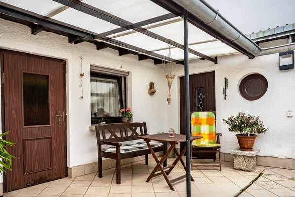 A patio with a wooden bench, a small table, a potted plant, and a door. - Studio Apartment 'Ferienzimmer Norbi Stralsund' with Private Terrace and Wi-Fi (Stralsund)