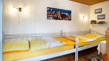Uma cama de solteiro com um edredom amarelo e branco, cabeceira branca e teto de madeira.
