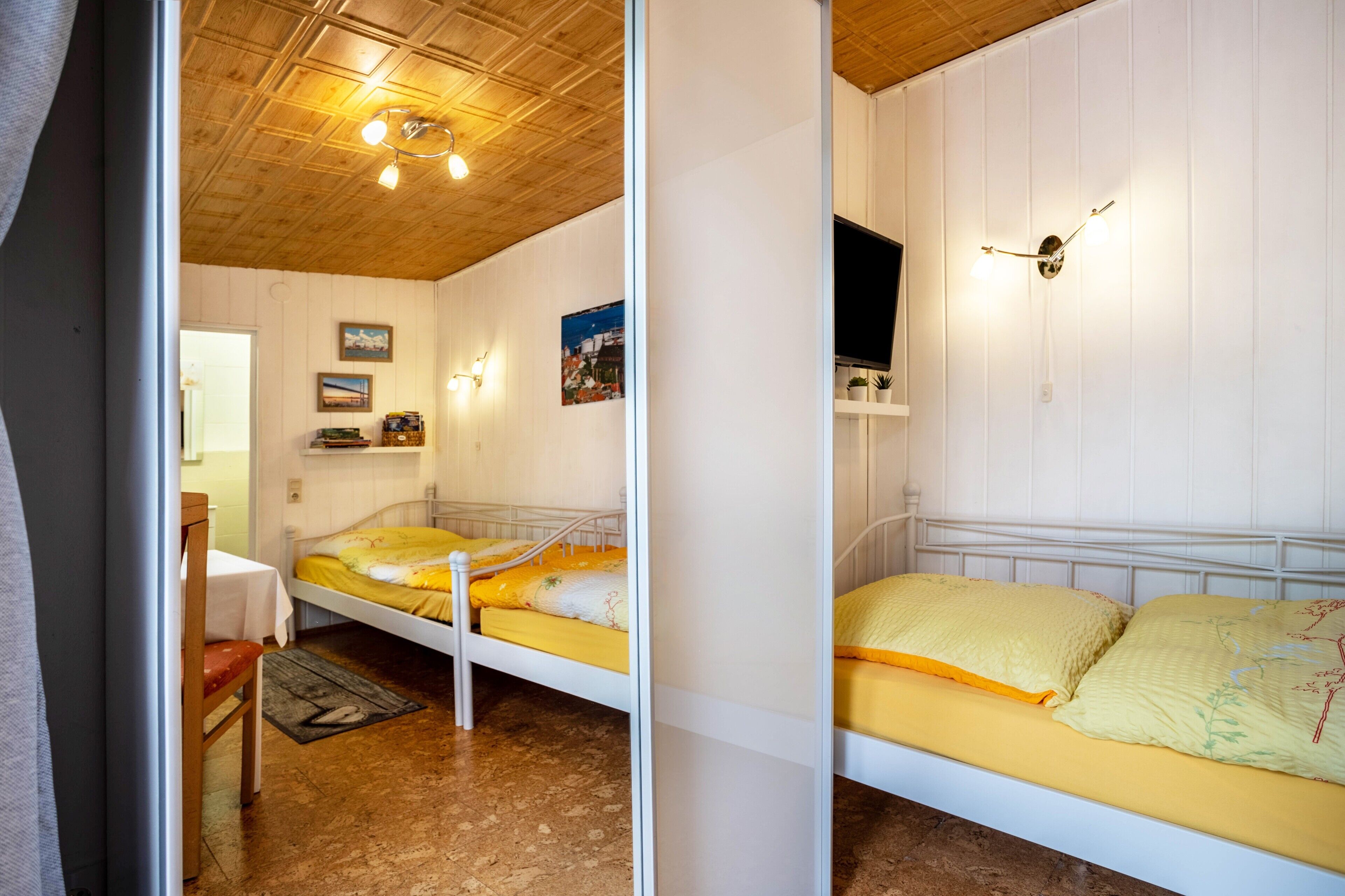 Una stanza con due letti, soffitto in legno, luci a parete e televisione.