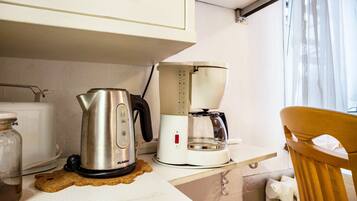 A kitchenette with a kettle, coffee maker, toaster, and a wooden chair.