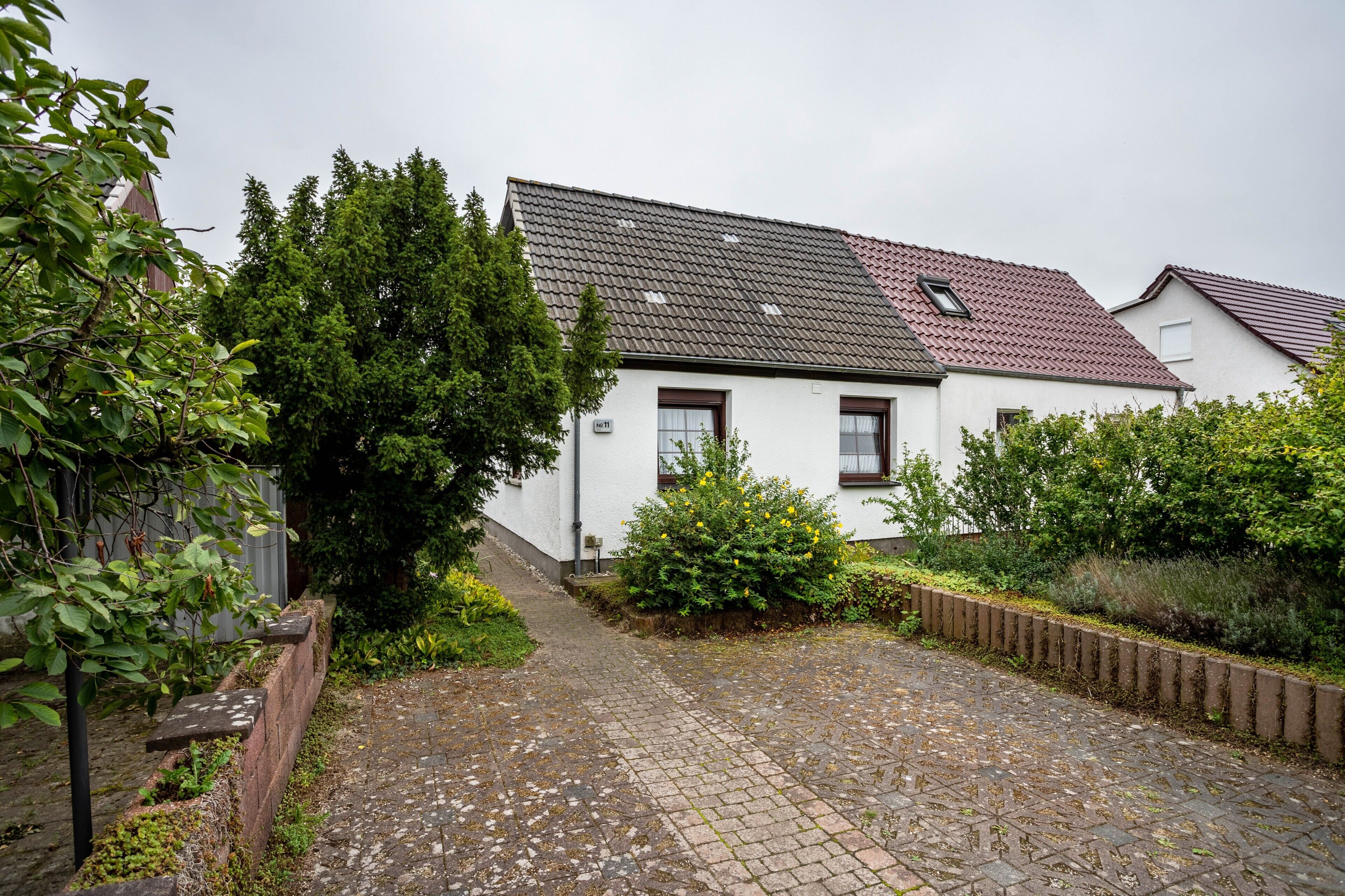 A white building with a red roof, a paved courtyard, and a wooden fence.
