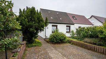A white building with a red roof, a paved courtyard, and a wooden fence.
