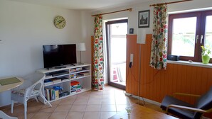A living room with a television, bookshelves, a chair, and a window with curtains.