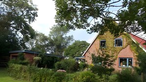 A house with a sloped roof, ivy-covered walls, and a garden with various plants and flowers.