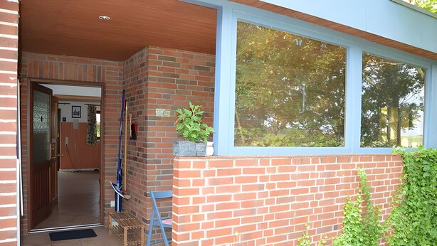 A brick building with a wooden door, a window, and a plant on the exterior wall.