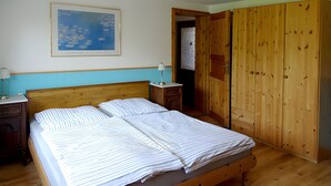 A bedroom with a wooden bed, a nightstand, a lamp, a wardrobe, and a framed picture on the wall.